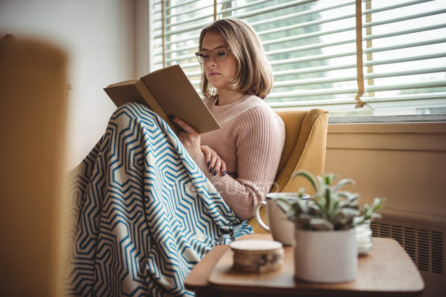Жінка сидить на стільці і читає книгу вдома — стокове фото