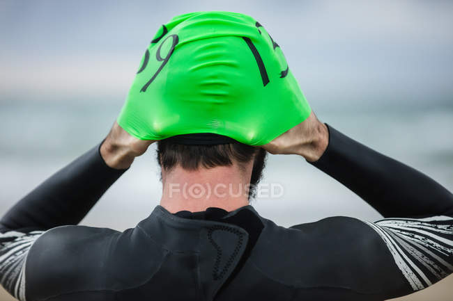 Вид сзади спортсмена в мокром костюме в плавательной шапке на пляже — стоковое фото