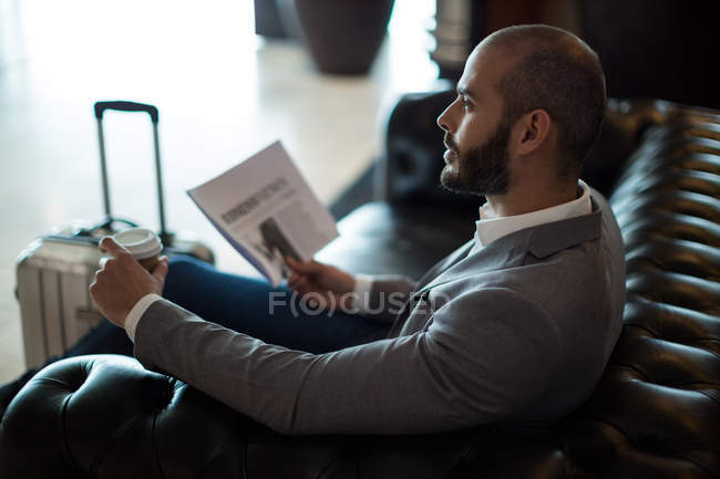 Pensativo empresario sosteniendo periódico y taza de café en la sala de espera en la terminal del aeropuerto - foto de stock
