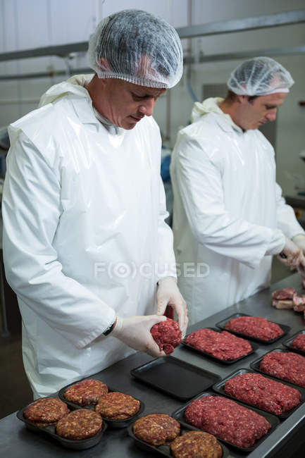 Carniceros organizando carne picada en bandeja de embalaje en fábrica de carne - foto de stock