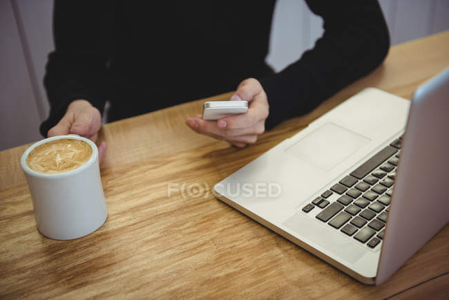Середній розділ людини, що використовує мобільний телефон, маючи каву в кав'ярні — стокове фото