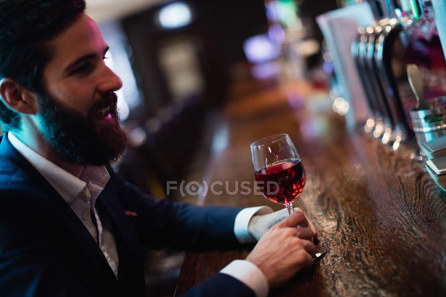 Hombre de negocios sonriente tomando una copa de vino en el mostrador en el bar - foto de stock
