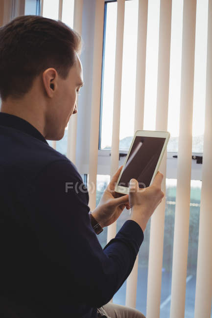 Männliche Führungskraft nutzt digitales Tablet in der Nähe von Jalousien im Büro — Stockfoto