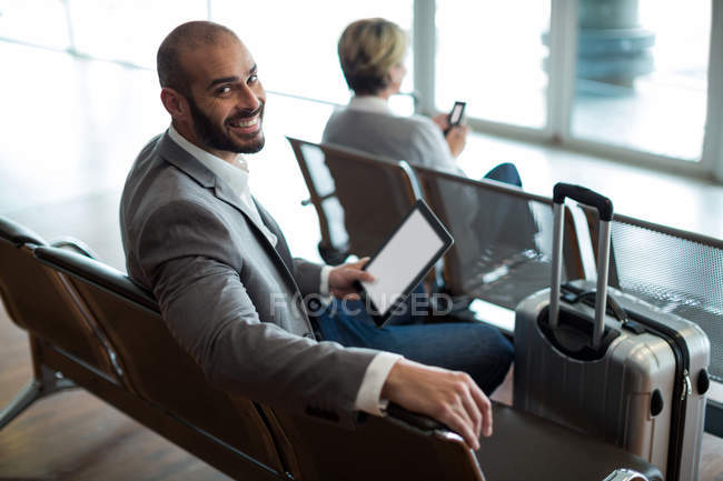 Retrato de un hombre de negocios sonriente con tableta digital sentado en la sala de espera en la terminal del aeropuerto - foto de stock