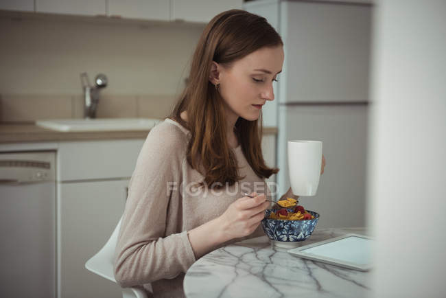 Женщина с цифровым планшетом во время завтрака на кухне дома — стоковое фото