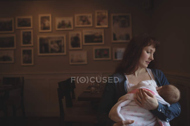 Мати середнього віку тримає милу дитину в руках у кафе — стокове фото