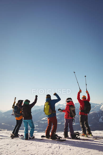 Vista trasera de los esquiadores celebrando de pie en las montañas cubiertas de nieve - foto de stock