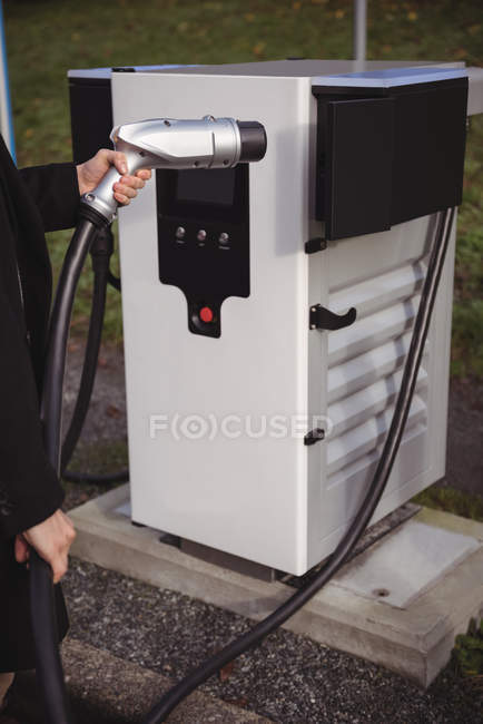 Средняя часть человека держит зарядное устройство на зарядной станции электромобиля — стоковое фото