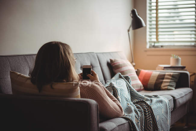 Женщина лежит на диване с помощью мобильного телефона в гостиной на дому — стоковое фото