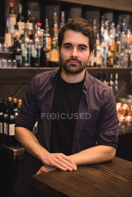 Retrato del camarero confiado parado en el mostrador del bar - foto de stock