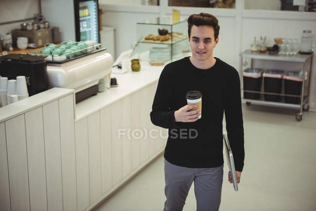 Homme avec ordinateur portable tenant une tasse de café jetable dans un café — Photo de stock