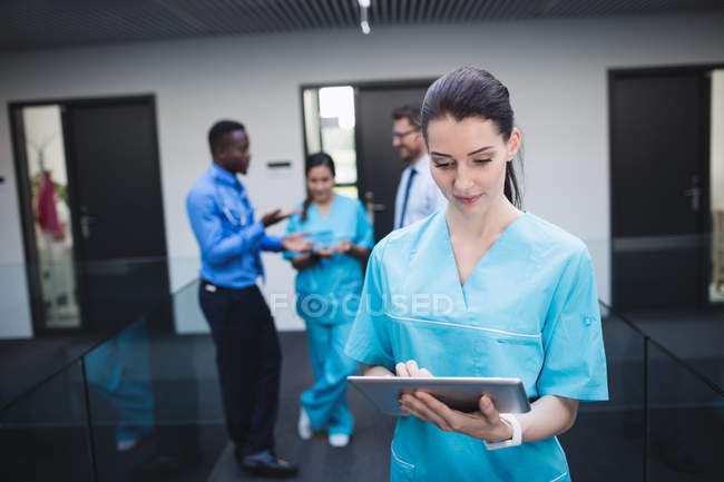Hermosa enfermera usando tableta digital en el pasillo del hospital - foto de stock