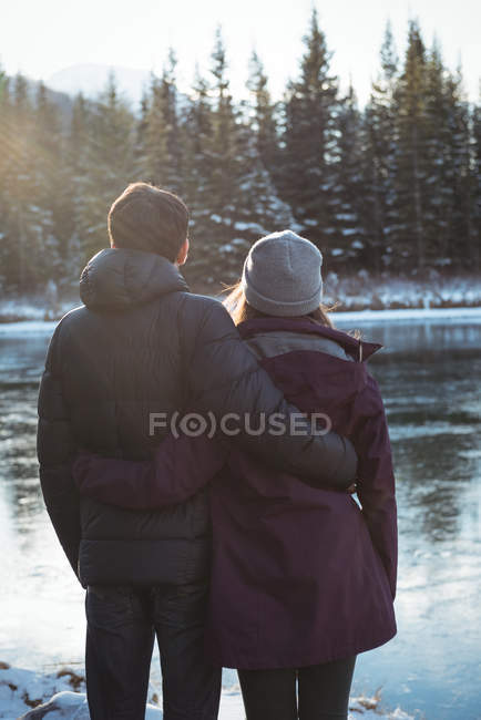 Vista trasera de pareja romántica de pie junto al río en invierno - foto de stock