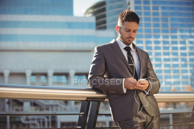 Uomo d'affari che ascolta musica e utilizza il telefono cellulare vicino all'edificio degli uffici — Foto stock