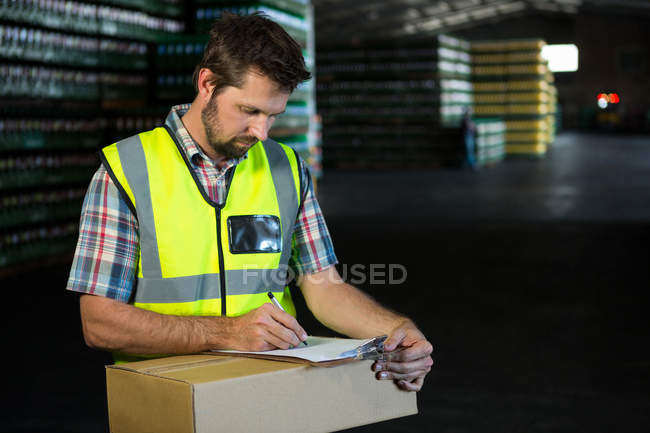 Confident male worker writing on clipboard in warehouse — Stock Photo