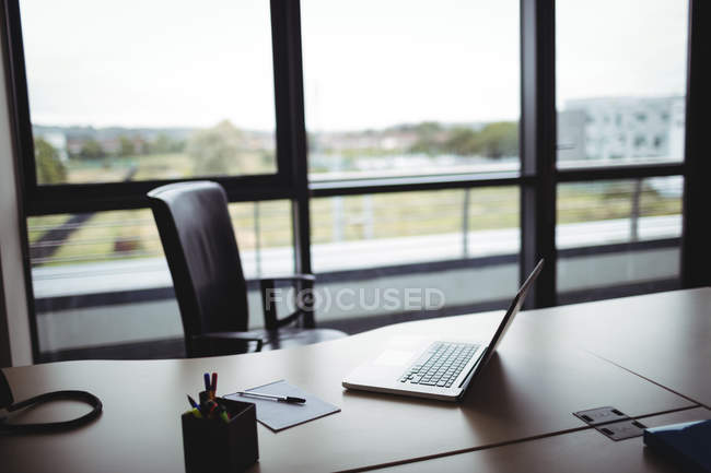 Laptop, suporte de caneta e bloco de notas na mesa no escritório moderno — Fotografia de Stock