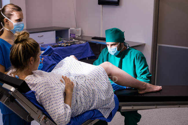 Equipo médico que examina a la mujer embarazada durante el parto en quirófano - foto de stock