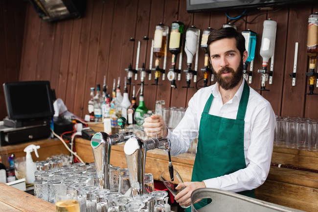 Portrait of bartender filling beer from bar pump at bar counter — Stock Photo