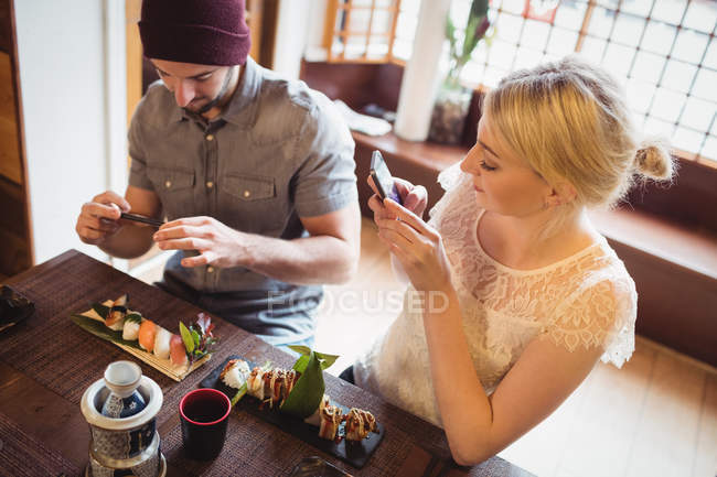 Pareja tomando fotos de sushi en el restaurante - foto de stock