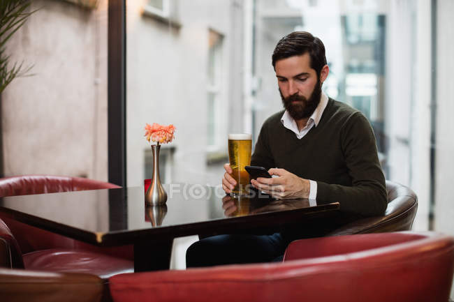 Чоловік використовує мобільний телефон, маючи келих пива в барі — стокове фото