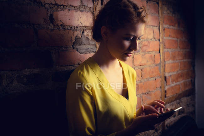 Жінка стоїть на цегляній стіні і використовує мобільний телефон — стокове фото