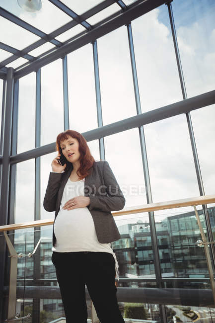 Donna d'affari incinta che parla al telefono cellulare vicino al corridoio in ufficio — Foto stock