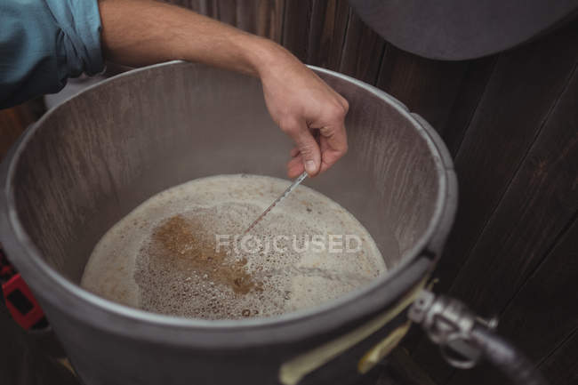 Primer plano del hombre probando la temperatura de la cerveza en mosto mientras hace cerveza en la cervecería casera - foto de stock