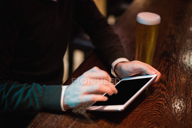 Homem usando tablet digital com copo de cerveja no balcão no bar — Fotografia de Stock