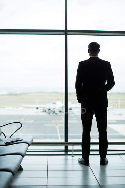 Vista posteriore dell'uomo d'affari che guarda attraverso la finestra in sala d'attesa in aeroporto — Foto stock