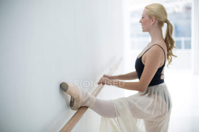 Bailarina que se estende em um barre enquanto pratica dança de balé no estúdio — Fotografia de Stock