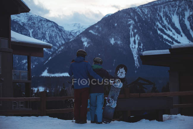Couple with snowboard standing on snow covered field against mountains — Stock Photo