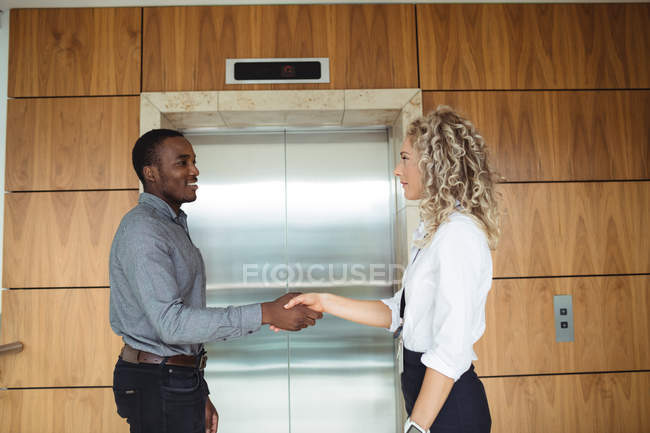 Business executives shaking hands near lift in office — Stock Photo