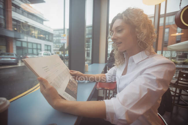 Mulher de negócios adulta média lendo jornal no balcão na cafetaria — Fotografia de Stock