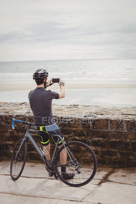 Visão traseira do atleta tirando foto no smartphone enquanto descansa na bicicleta — Fotografia de Stock