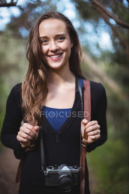 Усміхнена жінка стоїть з камерою в лісі — стокове фото