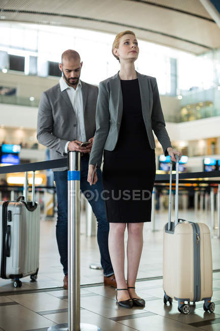Деловые люди ждут в очереди у стойки регистрации с багажом в терминале аэропорта — стоковое фото