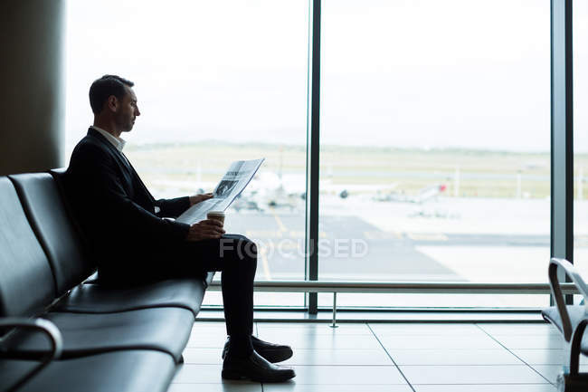 Uomo d'affari che prende un caffè mentre legge il giornale in sala d'attesa in aeroporto — Foto stock