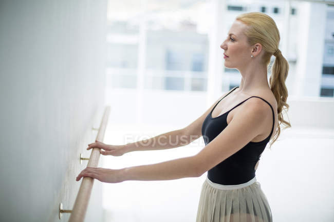 Bailarina que se estende em um barre enquanto pratica dança de balé no estúdio — Fotografia de Stock