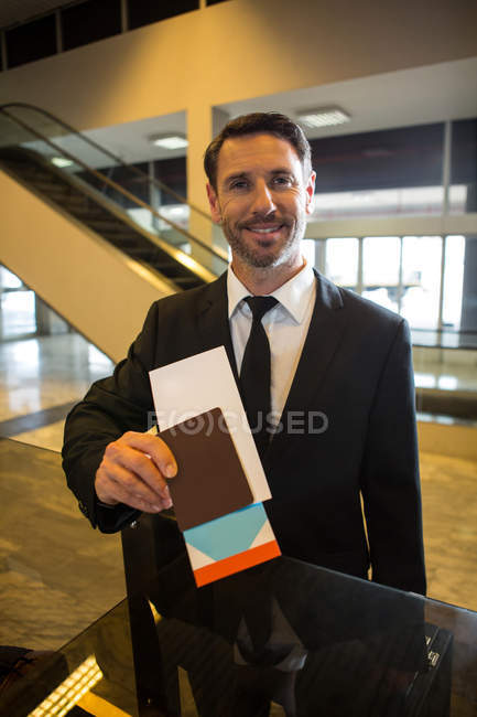 Портрет усміхненого бізнесмена, що показує посадковий талон в терміналі аеропорту — стокове фото
