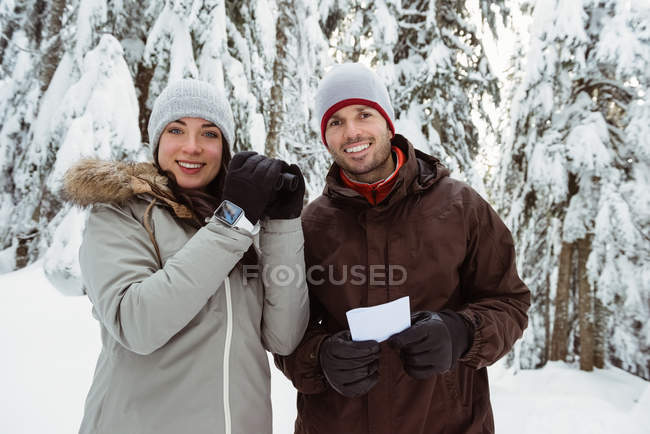 Retrato de una pareja de esquiadores sosteniendo un binocular y una tarjeta de dirección en la montaña cubierta de nieve - foto de stock