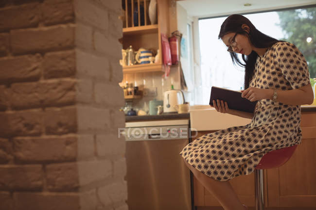 Mujer leyendo un libro en la cocina en casa - foto de stock