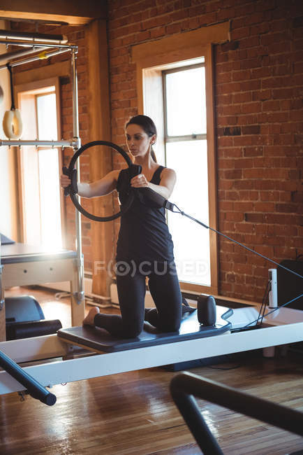 Mujer practicando pilates en reformador usando anillo de ejercicio en gimnasio - foto de stock