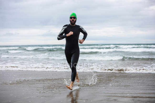 Портрет спортсмена в мокром костюме, бегущего по пляжу — стоковое фото