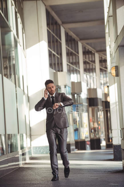 Бізнесмен розмовляє по мобільному телефону під час перевірки часу біля офісної будівлі — стокове фото