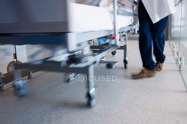 Section basse d'un médecin conduisant un patient au bloc opératoire sur une civière — Photo de stock