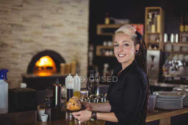 Portrait of waitress holding tray of muffins at counter in cafe — Stock Photo