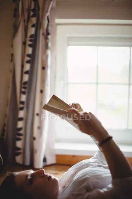 Mujer acostada en el suelo y leyendo un libro en casa - foto de stock