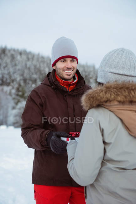 Mulher dando presente ao homem sorridente na montanha coberta de neve — Fotografia de Stock