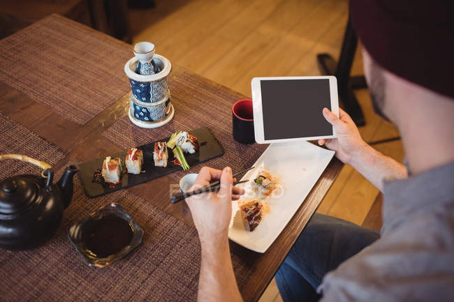 Чоловік використовує цифровий планшет під час їжі суші в ресторані — стокове фото