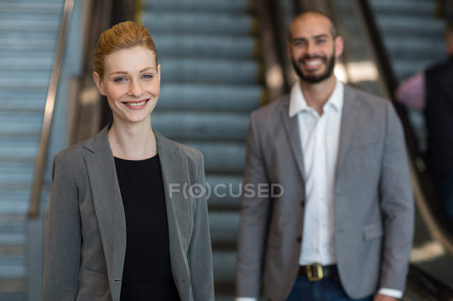 Lächelnde Geschäftsleute mit Gepäck vor einer Rolltreppe im Flughafenterminal — Stockfoto